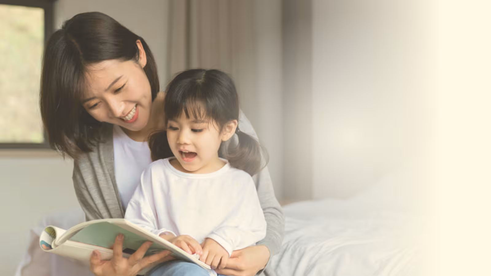 A parent and young child sitting on a bed, reading a picture book together